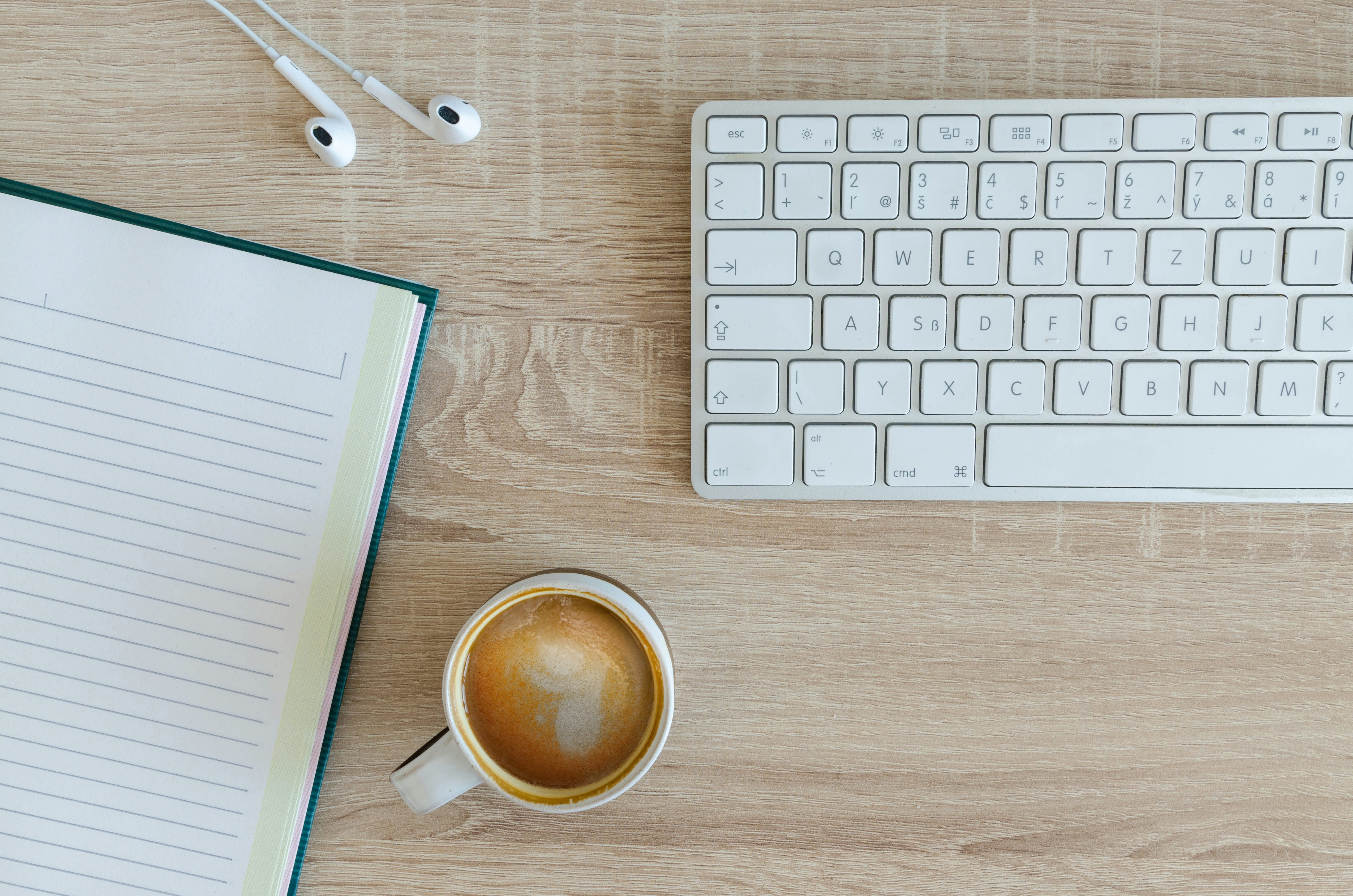 Mesa de trabajo con un café, un cuaderno, unos cascos y un teclado, representando un espacio de productividad y creatividad